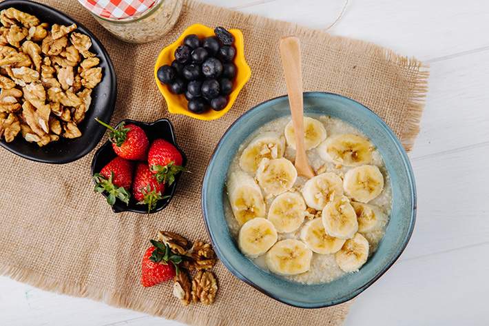 top-view-oatmeal-porridge-with-sliced-banana-ceramic-plate-fresh-strawberries-blueberry-nuts-sackcloth